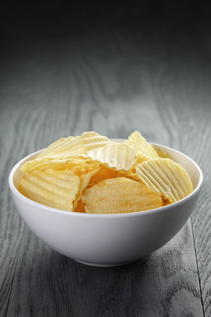 rippled organic chips in white bowl on wooden tableの写真素材