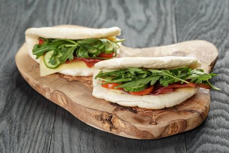 rustic sandwiches with ham arugula and tomatoes in pita bread, on wood tableの写真素材