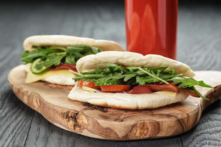 rustic sandwiches with ham arugula and tomatoes in pita bread and glass of juice, on wood tableの写真素材