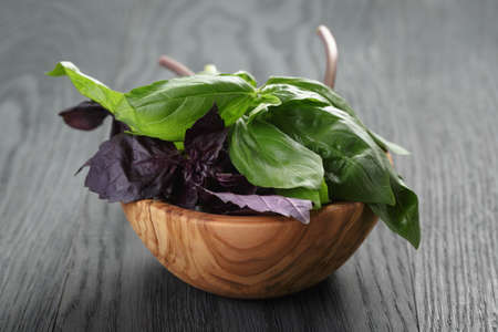 green and purple basil leaves in wood bowl on wooden tableの写真素材
