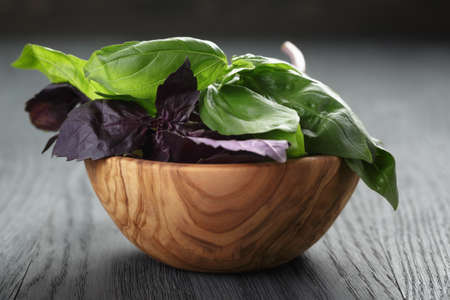 green and purple basil leaves in wood bowl on wooden tableの写真素材