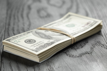 bunch of hundred dollar notes tied with rubberband on wood tableの写真素材