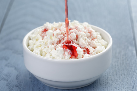 cottage cheese with strawberry jam in white bowl on blue wooden tableの写真素材