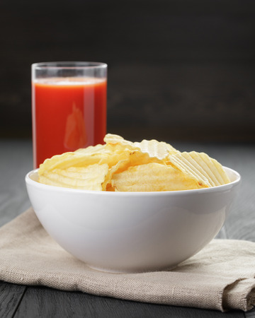 rippled organic chips in white bowl wit tomato juice on wooden tableの写真素材