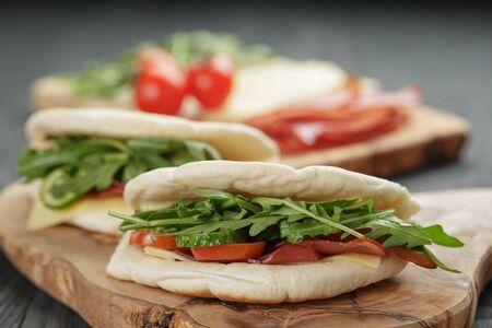 rustic sandwiches with ham arugula and tomatoes in pita bread, on wood tableの写真素材