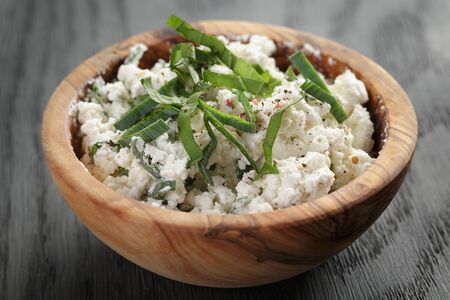 fresh ricotta with herbs in olive wood bowl on old tableの写真素材