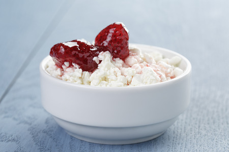 cottage cheese with strawberry jam in white bowl on blue wooden tableの写真素材