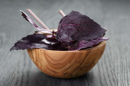purple basil leaves in wood bowl on wooden tableの写真素材