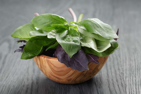 green and purple basil leaves in wood bowl on wooden tableの写真素材
