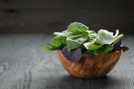 green and purple basil leaves in wood bowl on wooden tableの写真素材