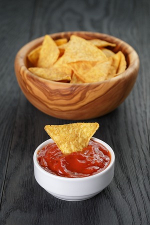 tortilla chips in olive wood bowl with tomato sauce on wooden tableの写真素材