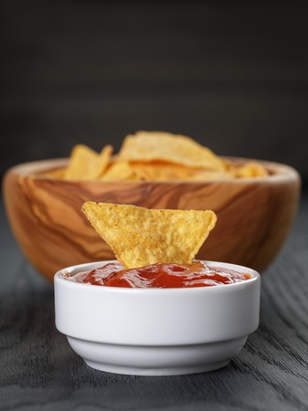 tortilla chips in olive wood bowl with tomato sauce on wooden tableの写真素材
