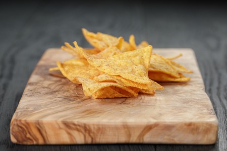 heap of tortilla chips on olive board on wooden tableの写真素材
