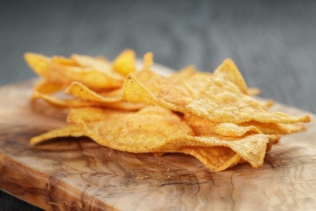 heap of tortilla chips on olive board on wooden tableの写真素材