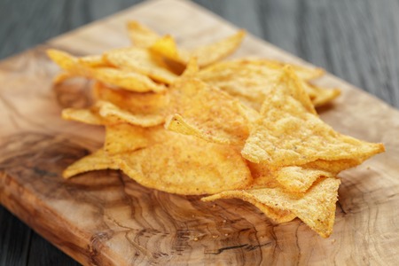 heap of tortilla chips on olive board on wooden tableの写真素材