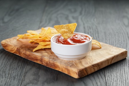tortilla chips on olive board with tomato sauce, on wooden tableの写真素材