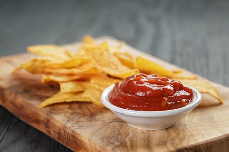 tortilla chips on olive board with tomato sauce, on wooden tableの写真素材