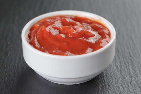 white bowl with tomato sauce on slate board, shallow focus