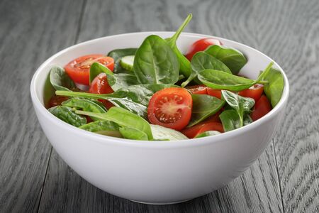 fresh summer organic salad with tomatoes cucumbers and spinach on wooden tableの写真素材