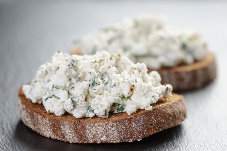 rye sandwiches or bruschetta with ricotta cheese and herbs on slate boardの写真素材