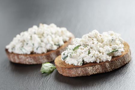 rye sandwiches or bruschetta with ricotta cheese and herbs on slate boardの写真素材