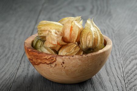 Physalis fruit in olive bowl on oak wooden table, closeup photoの写真素材