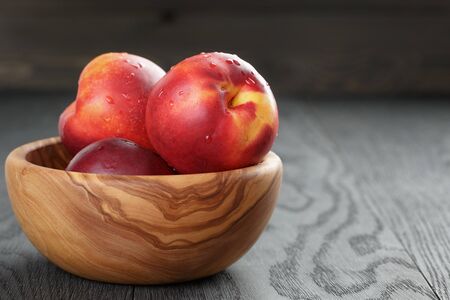 nectarines in olive wood bowl on oak table, shallow focusの写真素材