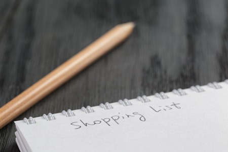 closeup photo of open empty notepad with shopping list phrase, on wood tableの写真素材