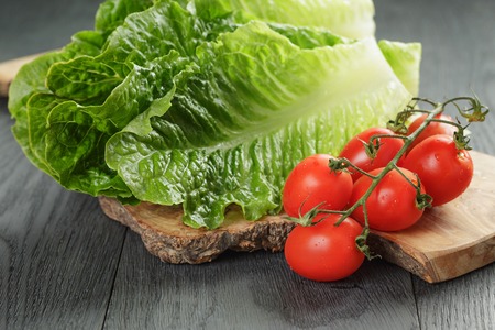 fresh romain green salad and tomatoes on olive board on wood table,の写真素材