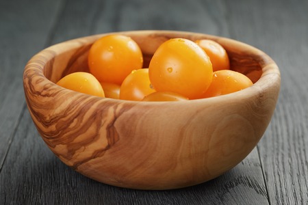 yellow cherry tomatoes in olive bowl on wood table, selective focusの写真素材