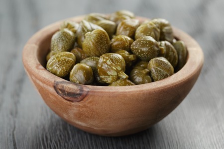 marinated capers in olive bowl on wood table, shallow focus
