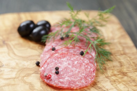 sliced salami with pepper on olive board on tableの写真素材