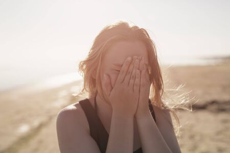 portrait of happy teen girl on beach closing her face with hands, summer photoの写真素材