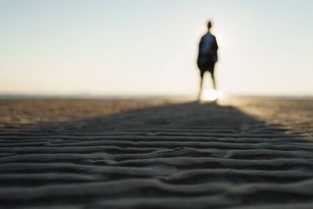 defocused photo of girl standing on beach, long shadowの写真素材