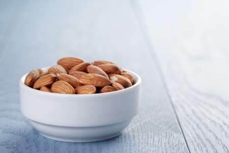 roasted almonds in white bowl on blue wooden tableの写真素材