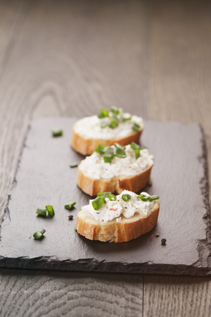crunchy baguette slices with cream cheese and green onion on slate boardの写真素材