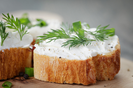 crunchy baguette slices with cream cheese and herbs on olive boardの写真素材