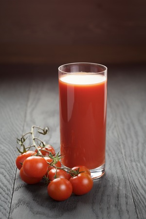 glass of tomato juice on wooden table with few tomatoesの写真素材