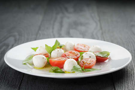 caprese salad with mini mozzarella balls and tomatoes, on old wood tableの写真素材
