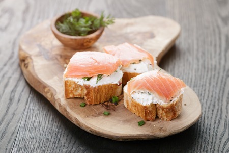 baguette slices with soft cheese and salmon on wood table, vintage tonedの写真素材