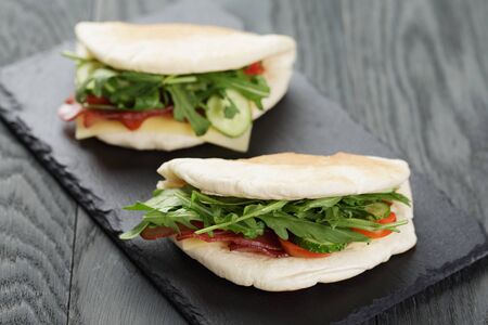 rustic sandwiches with ham arugula and tomatoes in pita bread on slate board