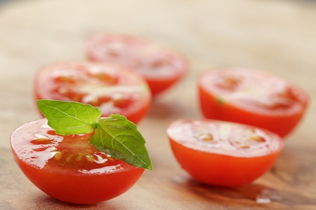 cut in half cherry tomatoes with basil leaf on wood table, shallow focusの写真素材