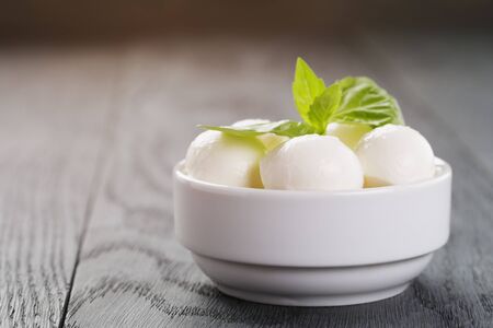 small balls of mozzarella in bowl with basil on wood tableの写真素材