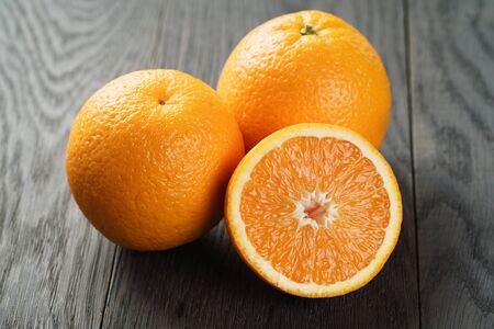 three ripe oranges on wooden table one half cut, shallow focusの写真素材