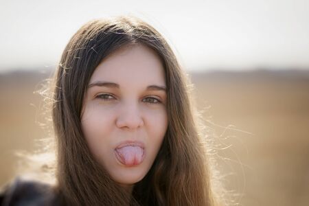 close up portrait of young girl showing tongue, outdoor photoの写真素材