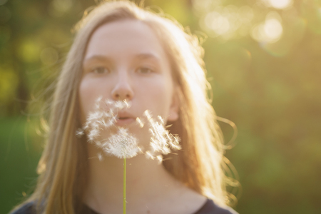 teen girl blowing dandelion to the camera, focus on dandelionの写真素材