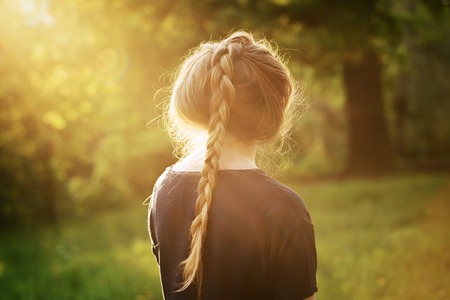 pretty teen girl standing and thining about something in park, from the back