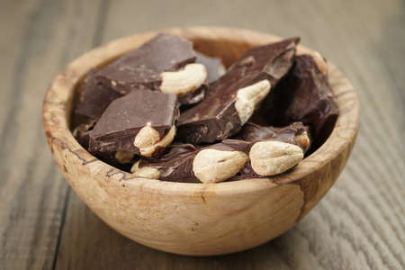 broken homemade bar of chocolate with cashew nuts in wood bowl, shallow depth of fieldの写真素材