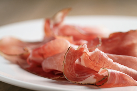 speck slices on white plate on old wood table, shallow focusの写真素材
