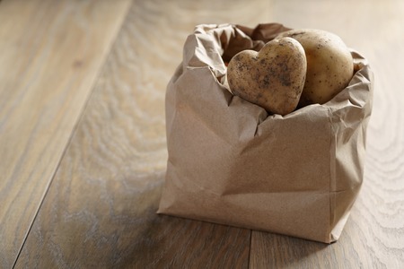 fresh potatoes in kraft paper bag on oak table, copy space for your info